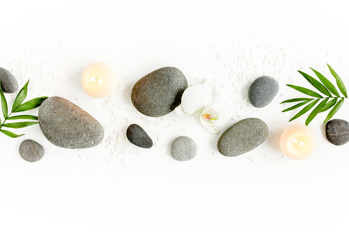 Spa stones, palm leaves, flower white orchid, candle and zen like grey stones on white background. Flat lay, top view. High quality photo