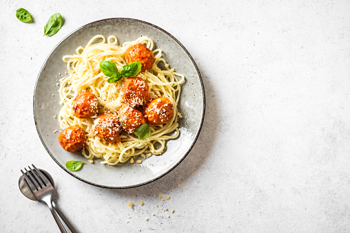 Spaghetti pasta with meatballs, tomato sauce, grated cheese and fresh basil - healthy homemade italian pasta on white background, top view, copy space.