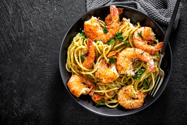 Spaghetti pasta with pesto and shrimps Tasty appetizing pasta spaghetti with pesto sauce and shrimps served in bowl on dark background. Top View with Copy Space. prawn seafood stock pictures, royalty-free photos & images