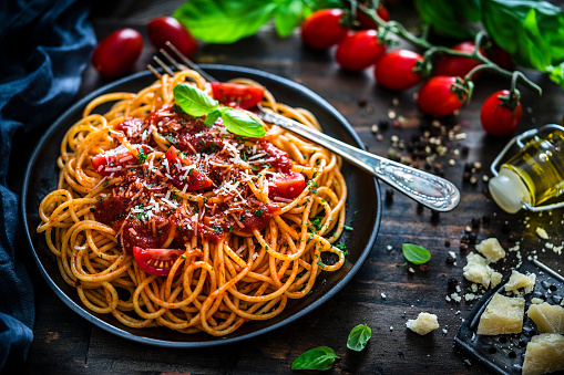 High angle view of spaghetti with tomato sauce plate shot on rustic wooden table. Some ingredients like ripe tomatoes, olive oil, basil, peppercorns and Parmesan cheese are all around the plate. XXXL 42Mp studio photo taken with SONY A7rII and Sony FE 90mm f2.8 Macro G OSS lens