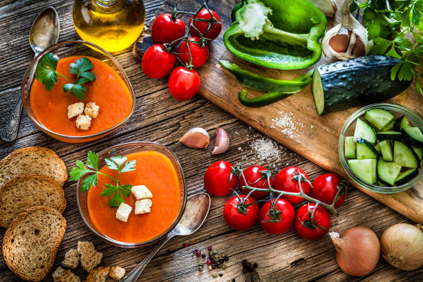 Spanish gazpacho and ingredients on rustic wooden table Two glass bowls filled with Spanish gazpacho soup shot from above on rustic wooden table. Ingredients like tomatoes, parsley, garlic, green bell pepper, cucumber, onions and olive oil complete the composition. Predominant colors are brown, green and red. DSRL studio photo taken with Canon EOS 5D Mk II and Canon EF 100mm f/2.8L Macro IS USM. mediterranean culture stock pictures, royalty-free photos & images