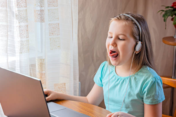 Speech training concept. Little girl uses a laptop to study at home with a teacher, a speech therapist. Speech training concept. Little girl uses a laptop to study at home with a teacher, a speech therapist. Distance learning. A kid doing exercises for correct pronunciation. healthy tongue stock pictures, royalty-free photos & images