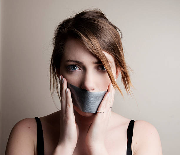 Speechless Photograph of a young woman with her mouth taped human mouth gag adhesive tape women stock pictures, royalty-free photos & images