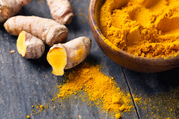 Spice: turmeric roots and powder on wood Freh turmeric roots and turmeric powder in a wooden bowl on rustic wood turmeric stock pictures, royalty-free photos & images