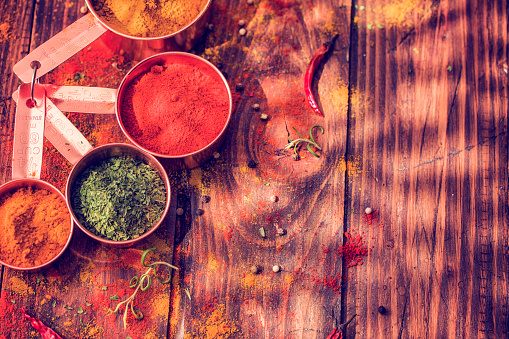 Variation of Spices and Herbs like chili peppers, parsley, rosemary, peppercorns, cayenne pepper, tumeric, cumin, fennel seeds on wooden background