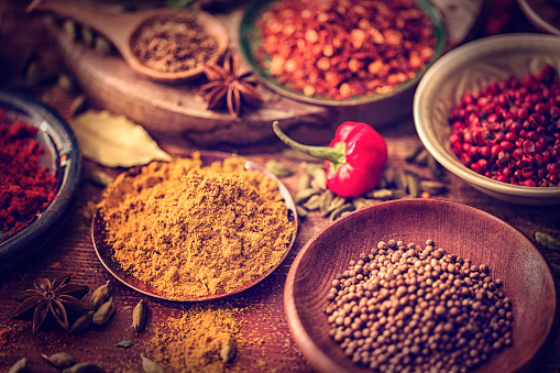Variation of Spices and Herbs like chili peppers, parsley, rosemary, peppercorns, cayenne pepper, tumeric, cumin, garlic and ginger on wooden background