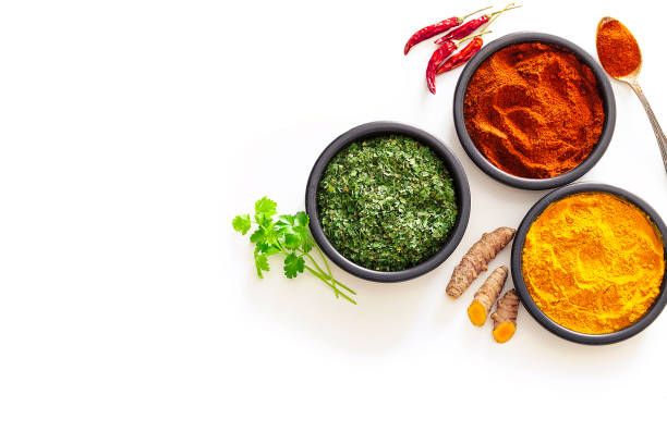 Spices: Turmeric, pepper powder and dried parsley shot from above on white background Spices: Indian food. Ground turmeric, chili pepper powder and dried parsley in black bowls shot from above on white background. The composition is at the right of an horizontal frame leaving useful copy space for text and/or logo at the left. High key DSRL studio photo taken with Canon EOS 5D Mk II and Canon EF 100mm f/2.8L Macro IS USM. condiment stock pictures, royalty-free photos & images