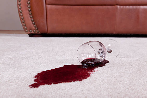 Spilled glass of wine on new carpet A wine glass with a red wine spill creating a puddle rests on a tan loop pile carpet.  The wine glass rests on the spilled wine.  The glass has a long stem and wide base.  The spill fans out from the top of the glass.  The spill appears deeper underneath the glass and then becomes a little lighter as it fans out.  The spill is oval in shape.  A tan leather couch with decorative metal buttons that run up the side sits in the background.  Neutral colored walls are also in the background. spilling stock pictures, royalty-free photos & images