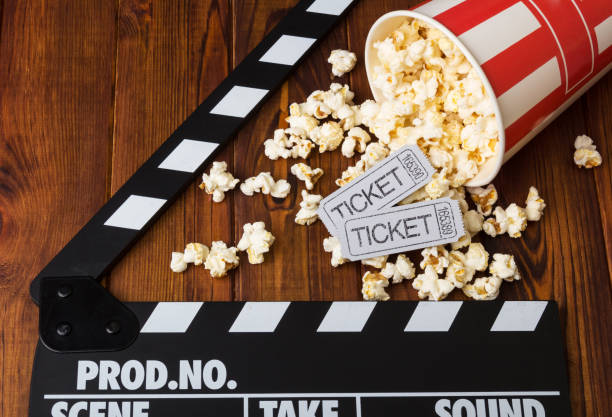 Spilled popcorn, striped box, movie tickets and movie clapper against dark wood. stock photo