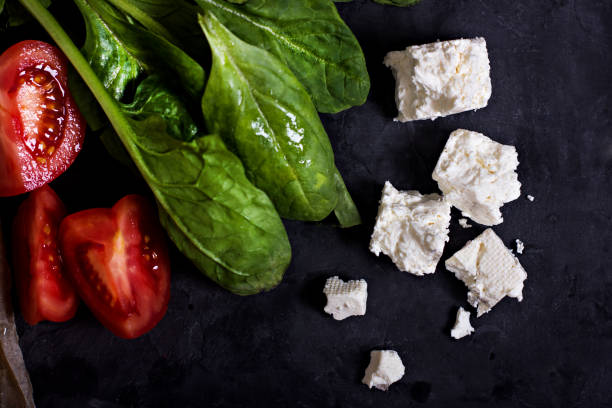 Spinach, cheese and tomatoes on a dark background. stock photo