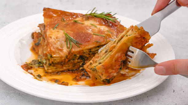 Spinach lasagna. Delicious spinach lasagna served with fresh rosemary close up on a plate on light grey background stock photo