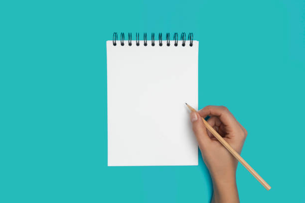 Spiral Notepad with Pencil Hand is holding pencil and is about to write something into a spiral notepad on blue background. aqua menthe photos stock pictures, royalty-free photos & images