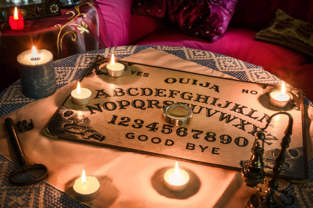 Spiritism table with a Ouija board Spiritism table with a Ouija board and many lighted candles. Esoteric seance on Halloween ouija board stock pictures, royalty-free photos & images