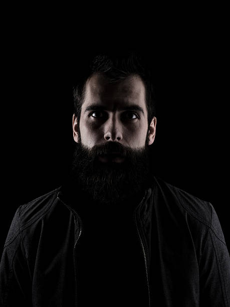 Spooky bearded man staring at camera Scary bearded man staring at camera. High contrast low key dark shadow portrait isolated over black background. chiaroscuro stock pictures, royalty-free photos & images