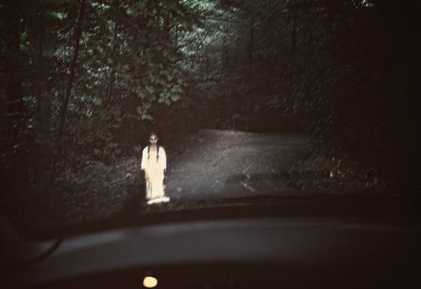 Spooky ghost in white standing in the middle of a dark road stock photo