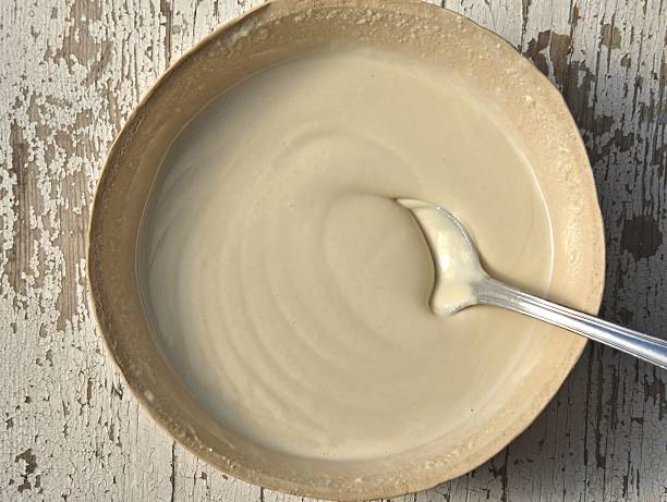 A spoon in bowl of creamy tahini, on a wooden table stock photo