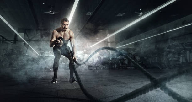 Sport. Battle ropes session. Attractive young fit sportswoman working out in functional training gym doing exercise with battle ropes. stock photo
