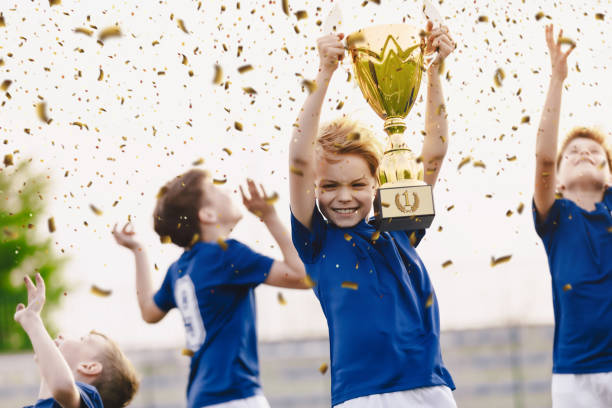 Sport team celebrating success. Happy boys rising golden trophy on celebration. Children winning sports soccer tournament competition. Inter-school soort competition Sport team celebrating success. Happy boys rising golden trophy on celebration. Children winning sports soccer tournament competition. Inter-school soort competition junior achievement stock pictures, royalty-free photos & images