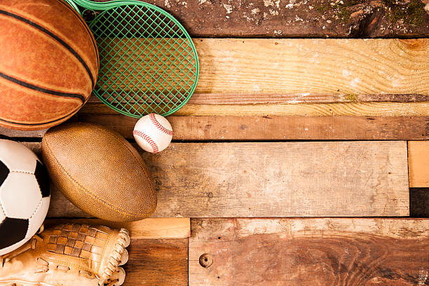 Sports concept. Basketball, tennis racket, baseball, glove, soccer ball, football to left of unique wooden boards background. Selective focus on wooden boards. 