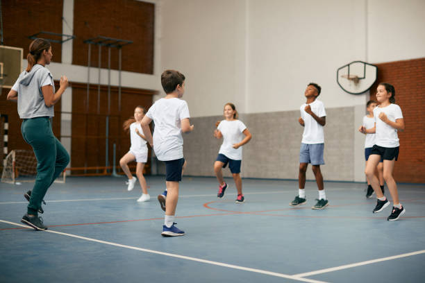 Sports teacher and group of kids exercising during physical activity class at school gym. stock photo