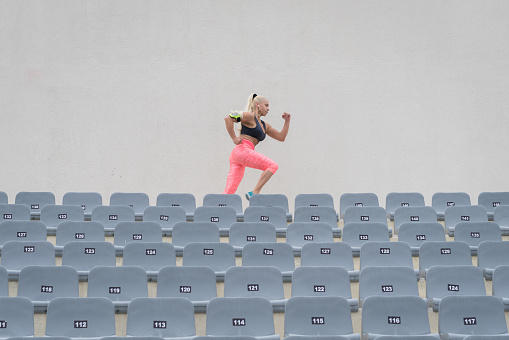 Female athlete running up the stairs of a stadium. Woman in fitness wear doing workout running on stairs beside the seats of a stadium.
