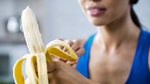 Sports woman peeling sweet banana for snack, hungry after active workout in gym stock photo