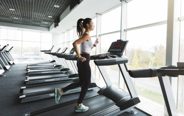 pelatihan wanita olahraga di treadmill dekat jendela - treadmill potret stok, foto, & gambar bebas royalti