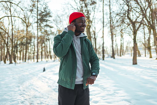Young African man exercising in the forest on winter day, Sportsman putting his headphones in his ears in the park.