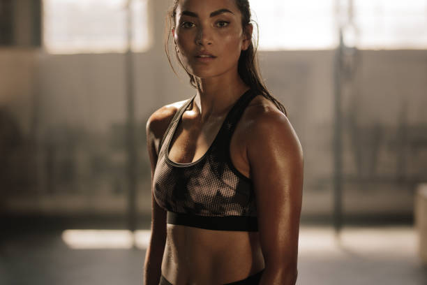 Sportswoman after intense crossing training session Strong and determined female in sportswear standing in the gym and looking at camera. Sportswoman after intense crossing training workout session in gym. toughness stock pictures, royalty-free photos & images
