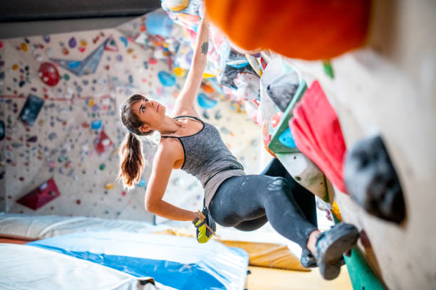 Sportswoman Reaching into Chalk Bag on Bouldering Wall Side view of Caucasian female climber in early 20s gripping hand and foot holds while working out on bouldering wall in modern sport climbing center. bouldering stock pictures, royalty-free photos & images
