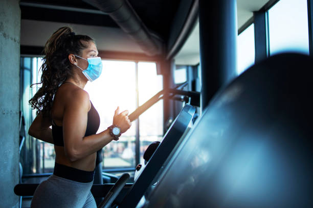 sportvrouw opleiding op loopband in de sportschool en het dragen van gezichtsmasker om zichzelf te beschermen tegen coronavirus tijdens de wereldwijde pandemie van covid-19 virus. - fitness stockfoto's en -beelden