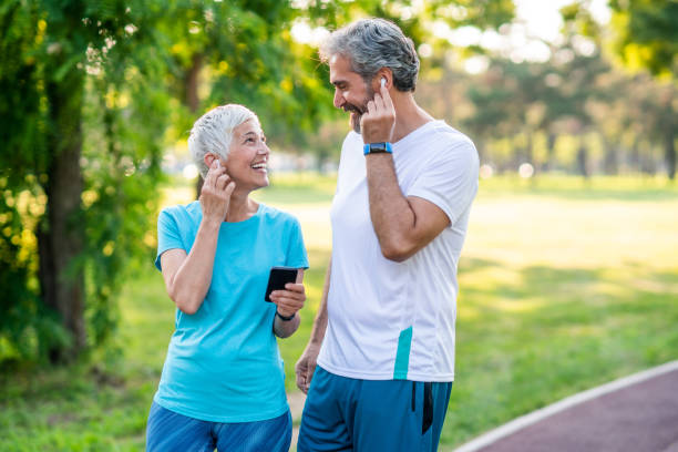 Sporty couple jogging Smiling mature couple in sports wear jogging together. Using smartphone and touching their in-ear headphones. 50 59 years stock pictures, royalty-free photos & images