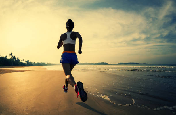 Sporty fitness woman runner running on sunrise beach stock photo