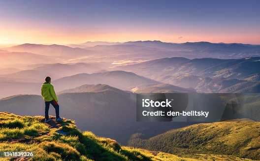 istock Sporty man on the mountain peak looking on mountain valley with sunbeams at colorful sunset in autumn in Europe. Landscape with traveler, foggy hills, forest in fall, amazing sky and sunlight in fall 1341839326