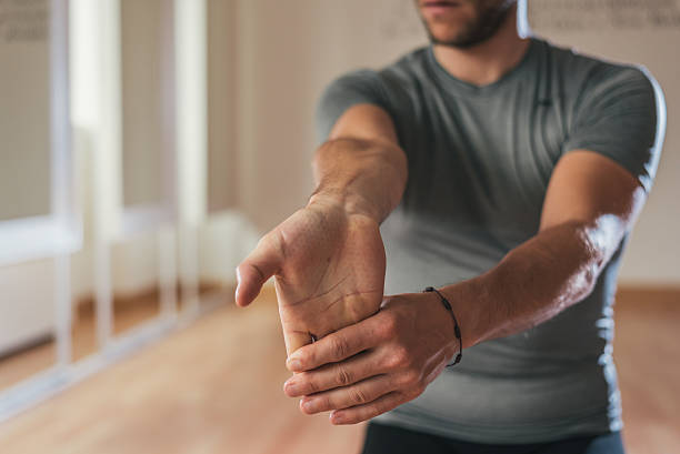 Sporty man stretching forearm before gym workout Sporty man stretching forearm before gym workout. Fitness strong male athlete standing indoor warming up. human arm stock pictures, royalty-free photos & images