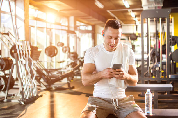 Sporty man with earphones using mobile phone and listening to music at gym. stock photo