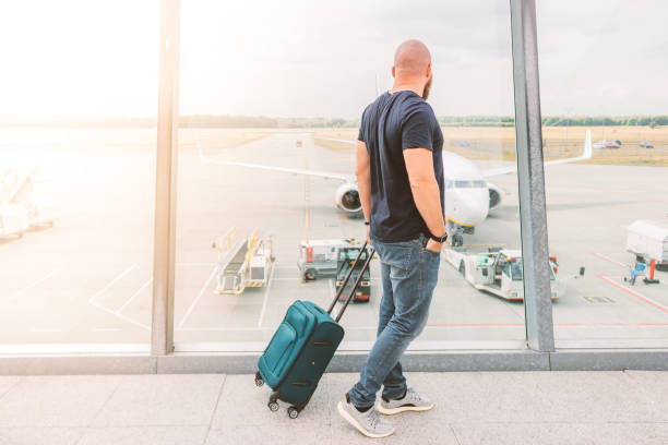 Sporty man with shaved head and beard is observing an airplane preparation while waiting his flight. Sunny warm shot.  broken suitcase stock pictures, royalty-free photos & images