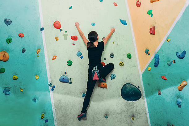 Sporty woman climbing up on practice rock wall indoor Young sporty woman climbing up on practice rock wall in gym, rear view bouldering stock pictures, royalty-free photos & images