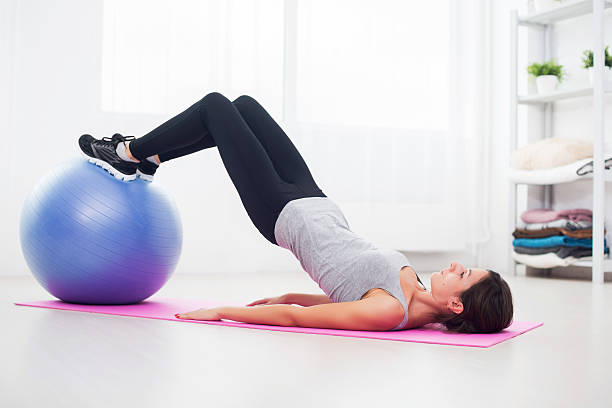 sporty woman doing pilates exercise lifting her pelvis with fit sporty woman doing pilates exercise lifting her pelvis with fit ball at home pelvis stock pictures, royalty-free photos & images