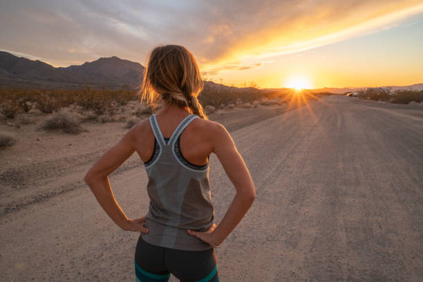 Sporty young woman contemplating sunset at the end of the road; female stretches body in nature  USA stock photo