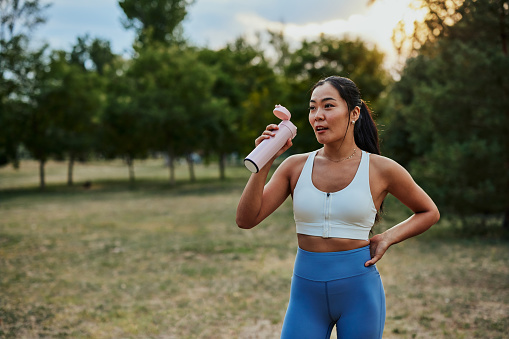 Woman drinking water from bottle. Asian female drinking water after exercises in the park