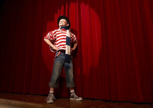 spotlight on boy (8-10) in clown outfit, hands on hips, low angle view - artiest stockfoto's en -beelden