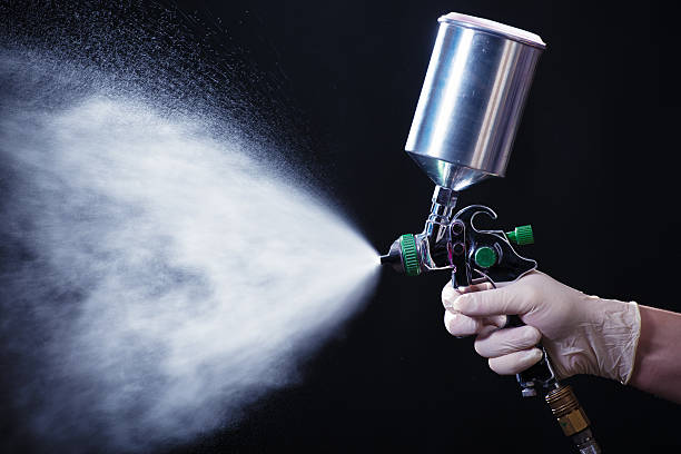 Spray gun in hand Painter painting with spray gun. Dark background. airbrush stock pictures, royalty-free photos & images