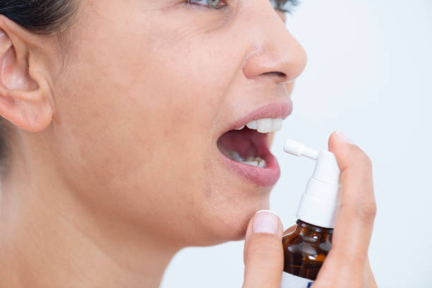 Spray Medicine Mid adult woman spraying medicine in mouth. bad breath stock pictures, royalty-free photos & images