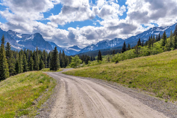 Spring Mountain Road - A dirt country road winding in Cut Bank Valley towards high peaks of Lewis Range on a sunny Spring Evening in Glacier National Park. stock photo