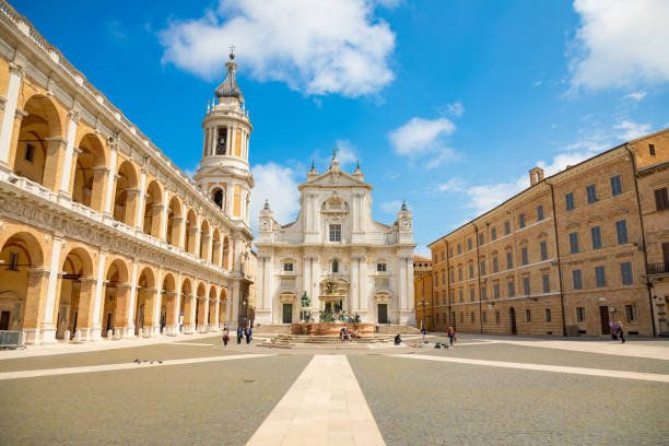 Square of Loreto with background the basilica in sunny day, portico to the side, people in the square in Loreto Loreto, Ancona, Italy - May 9, 2018: Square of Loreto with background the basilica in sunny day, portico to the side, people in the square in Loreto, Italy pilgrims monument stock pictures, royalty-free photos & images