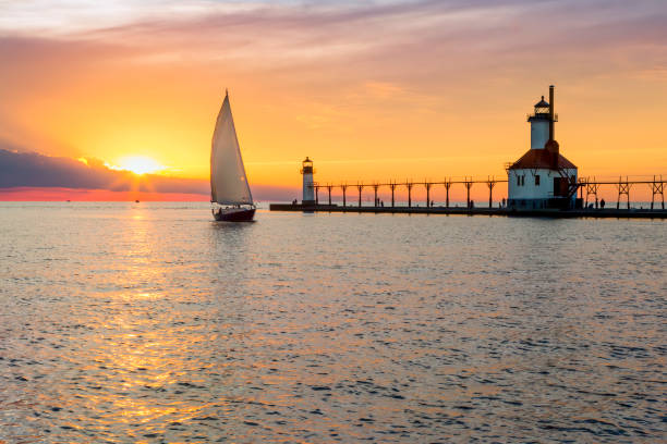 St. Joseph Lighthouse and Sailboat Solstice Sundown A sailboat rounds the breakwater near sunset on the longest day of the year by the Lighthouses at St. Joseph, Michigan with people fishing from and walking on the pier. great lakes stock pictures, royalty-free photos & images