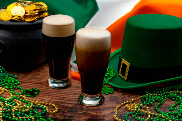 St Patrick's day party and Irish celebration of patron saint concept theme with frothy glasses of dry stout, green hat with a buckle, a pot of gold, the flag of Ireland and beads with shamrock in a pub stock photo