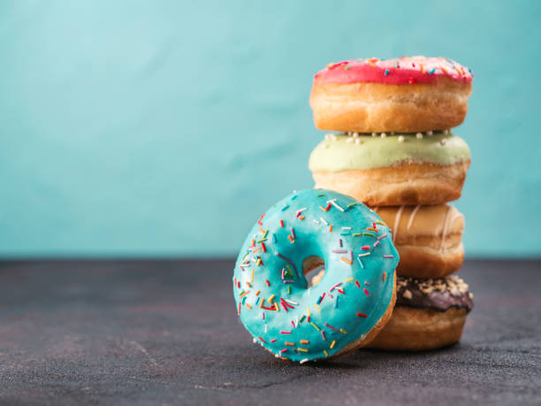 Stack of assorted donuts, copy space Stack of assorted donuts on black and blue cement background. Blue glazed doughnut with sprinkles on foreground. Copy space. Shallow DOF doughnut stock pictures, royalty-free photos & images