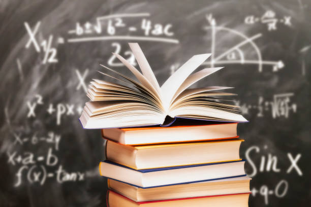 Stack of books in front of a blackboard Opened book on a stack in front of a blackboard with mathematical formulas math stock pictures, royalty-free photos & images